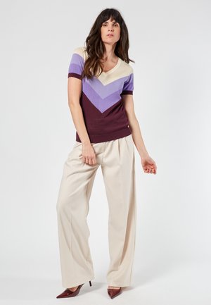 V-neck knit top with purple and cream chevron stripes, paired with cream wide-leg trousers and burgundy pointed heels. Smooth texture and fitted design.