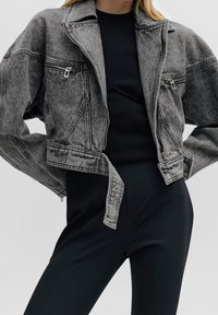 Grå denim kort jacka med en dragkedjeficka, kontrasterande sömmar och nitar. Matchad med en svart ribbad tröja och byxor.