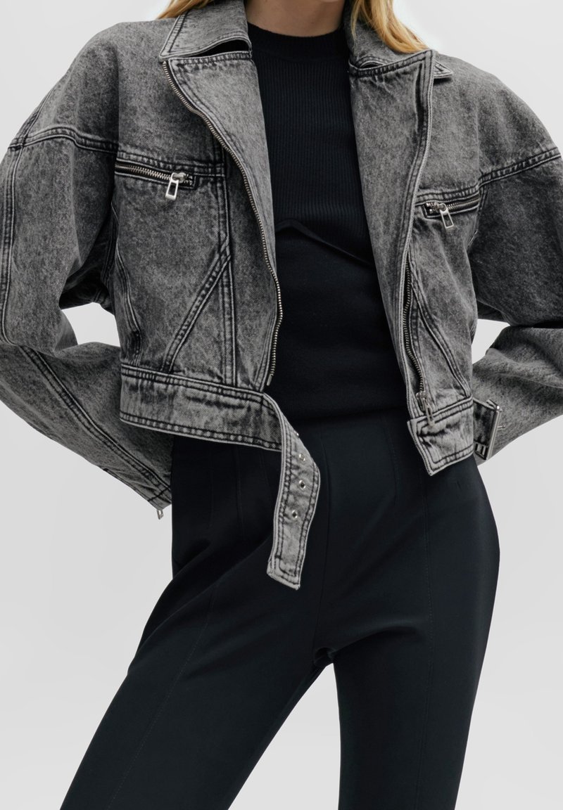 Grå denim kort jacka med en dragkedjeficka, kontrasterande sömmar och nitar. Matchad med en svart ribbad tröja och byxor.