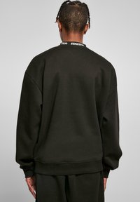 Sort sweatshirt med rund halsudskæring og ribbede manchetter, med 'STARTER' logo-bånd ved kraven. Blødt, struktureret stof, afslappet pasform.