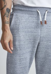 Grå bomulls joggebukser med en myk tekstur, som har ribbestrikket midjebånd, hempesnor med lærdetaljer og sidelommer.