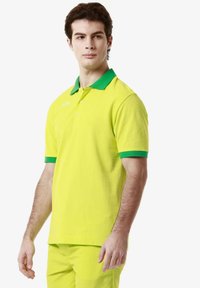 Polo di un brillante colore giallo con colletto e rifiniture delle maniche verdi. Realizzato in cotone, presenta una vestibilità classica e una chiusura con tre bottoni.