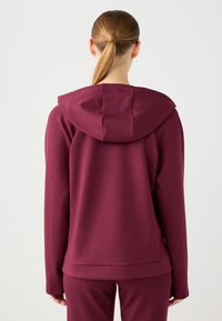 Burgundowa bluza z kapturem z regulowanym ściągaczem, miękka w dotyku, z długimi rękawami. Posiada luźny krój oraz detal w postaci wentylacji z tyłu. Zaprojektowana z myślą o komforcie.