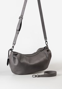 Grau farbene Leder-Schultertasche mit verstellbarem Tragegurt, die hängt, Reißverschlussverschluss und einem abnehmbaren Handgelenkstrap, der darunter platziert ist.