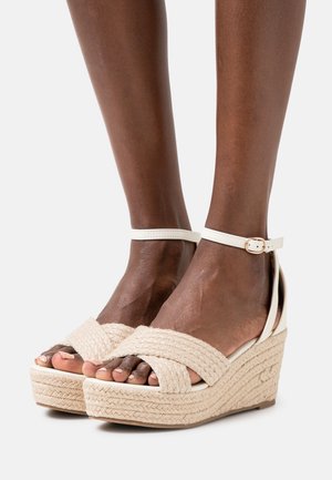 Wedge sandals with a natural woven jute platform and a white ankle strap. The upper features crisscrossed textured fabric.