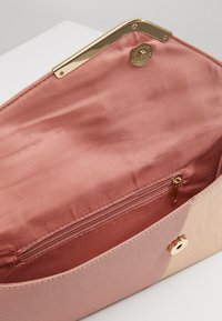 Kabelka v růžovém zlatě s lesklým zlatým klipem, uvnitř s růžovým saténem a s kapsou na zip pro lepší organizaci.