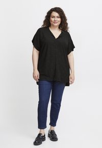 Sort kortærmet top med V-hals og struktureret stof, parret med mørkeblå slim jeans og sorte loafers. Enkelt, afslappet design.
