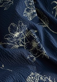 Marineblaues Gewebe mit strukturierter Oberfläche, das weiße Blumenmuster und Umrisse aufweist und ein dezentes, filigranes Design schafft.
