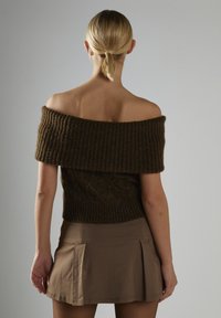 Brązowy sweter dzianinowy na ramiączkach z prążkowanymi detalami i teksturowanym korpusem, zestawiony z brązową spódnicą plisowaną.
