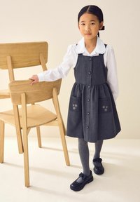 Grijs denim jurk met knopen, uitlopende rok en bloemrijke zakken, gecombineerd met een witte blouse met kraag en grijze panty, tegen een neutrale achtergrond.