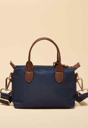 Tummansininen käsilaukku, jossa on ruskeat nahkahihnat ja kullanväriset metalliosat, irrotettava olkahihna ja vetoketjullinen yläkiinnitys.