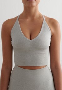 Sostén deportivo gris acanalado con un diseño de escote en V y tirantes delgados. El material parece suave y elástico, con una textura lisa y una silueta ajustada.
