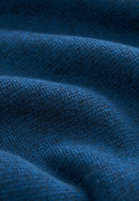 Modrý textil s jemným, texturovaným povrchem, který má tkaný vzor a jemné barevné variace, vytvářející hloubku a vizuální zajímavost.