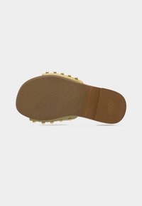 Sandale jaune avec une semelle texturée marron, ornée de clous dorés le long du bord. Design plat avec un bout ouvert et un talon minimal.