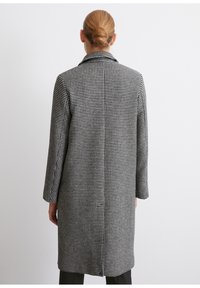 Palton cu model houndstooth alb-negru, cu guler cu vârf, mâneci lungi, croială dreaptă și detalii subtile ale cusăturii pe spate.
