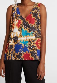 Flerfärgad ärmlös topp med V-hals, intrikata guldmönster, prickar och livliga block av röd, blå och svart.
