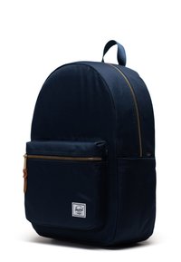 Zaino in tessuto blu navy con forma arrotondata, con dettagli in cerniera dorata, una tasca frontale e una maniglia superiore per il trasporto. Presenta un'etichetta con logo.