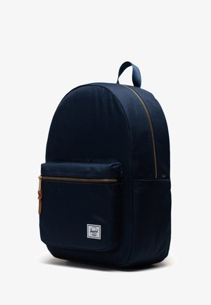 Merenneitokankainen reppu pyöreällä muodolla, kultaisilla vetoketjuyksityiskohdilla, edessä oleva tasku ja yläkahva kantamista varten. Ominaisuuksiin kuuluu logopatch.