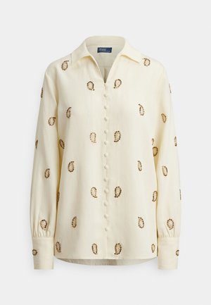 Svijetložuta bluza s ovratnikom, s smeđim paisley vezom i zatvaranjem na prednje gumbe. Dugih rukava s naboranim manšetama.