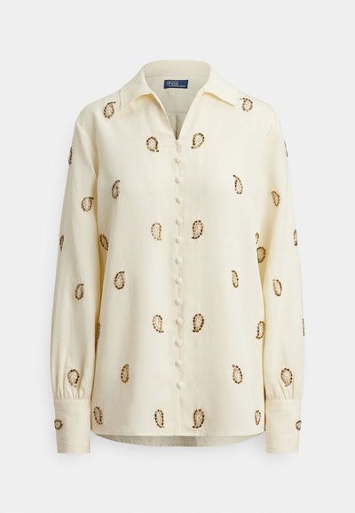 Svetložltá blúzka s golierom, zdobená hnedou paisley výšivkou a zapínaním na gombíky vpredu. Dlhé rukávy so zaviazanými manžetami.