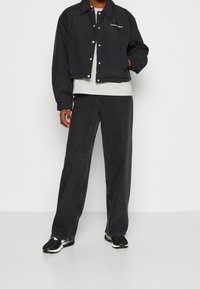 Sort cropped pufferjakke med sølvfarvede trykknapper, der har en forlommer og logo. Sammen med mørke vide jeans og sorte sneakers.
