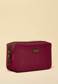 Kosmetyczka Joules w kolorze fuksji z teksturowanym wykończeniem, brązowym suwakiem i naszywką z logo. Prostokątny kształt wykonany z trwałego, wodoodpornego materiału.