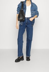 Chaqueta de mezclilla azul sobre una camiseta blanca, combinada con unos jeans azul de cintura alta y zapatos negros de suela gruesa. Incluye un bolso de cuero negro.