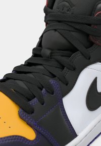 Κοντινό ενός αθλητικού παπουτσιού σε μαύρο, λευκό, μοβ και κίτρινο, με μαύρα κορδόνια και μαύρο λογότυπο Nike στην πλευρική επιφάνεια.