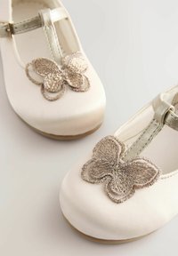 Weiße Satin Schuhe mit runder Zehenpartie, goldenen Schmetterlingsstickereien und einem silbernen Riemen. Flache Sohle und glatte Textur.