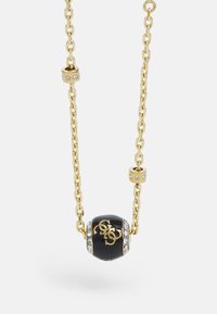 Collar de cadena de oro con una cuenta negra que presenta un diseño de logo y acentos de rhinestones, mostrando una textura suave y una forma redondeada.