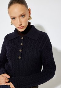 Marineblaue Zopfmustersweatshirt mit weitem Kragen, ausgestattet mit sechs goldfarbenen Knöpfen und gerippten Bündchen. Glatte Textur mit taillierter Silhouette.