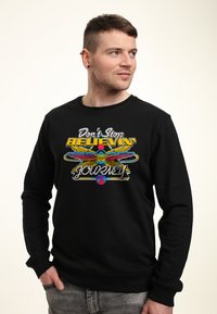 Svart sweatshirt med rund halsringning som har en färgstark grafisk design. Noterbara inslag inkluderar text och stiliserade bilder. Mjuk textur.