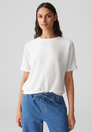 White short-sleeve top featuring a textured pattern and round neckline, paired with blue drawstring pants.