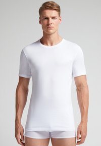 Bílý krátký rukáv tričko vyrobené z prodyšného materiálu. Obsahuje kulatý výstřih, hladkou texturu a slim fit, nošené s bílými trenýrkami.