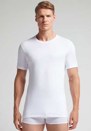 Weiße kurzärmlige T-Shirt aus atmungsaktivem Material. Mit einem Rundhalsausschnitt, glatter Textur und schmaler Passform, getragen mit weißen Slips.