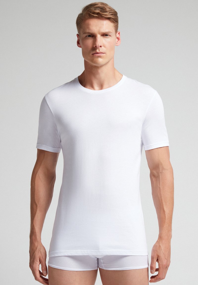 Bílý krátký rukáv tričko vyrobené z prodyšného materiálu. Obsahuje kulatý výstřih, hladkou texturu a slim fit, nošené s bílými trenýrkami.