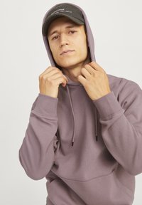 Light purple hooded sweatshirt with drawstrings, ribbed cuffs, and a front pocket. Worn with a black cap featuring white text.