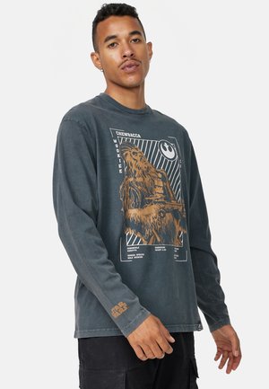 Langærmet, mørkegrå t-shirt med et slidt Chewbacca grafik i brunt, med hvid tekst og et Star Wars-logo detaljeret på ærmet.