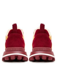 Paire de baskets en daim rouge avec semelles épaisses à crampons et doublure en fourrure, vues de dos sur fond blanc.