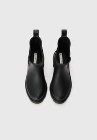 Bottes en caoutchouc noires à la cheville avec une finition lisse, des panneaux latéraux élastiques et des languettes au niveau des talons pour un enfilage facile. Pas de motifs ni d'accents visibles.