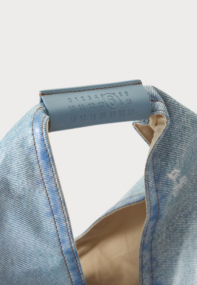 Τσάντα tote ανοιχτού μπλε denim με καφέ ραφές και μπλε δερμάτινη λαβή με χαραγμένους αριθμούς από το 0 έως το 23 και έναν αριθμό 6 μέσα σε κύκλο.