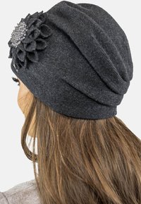 Berretto in maglia grigio scuro con un fit slouchy, dotato di un fiore in feltro texturizzato e un accento di strass. Materiale morbido e caldo, adatto per il clima più freddo.