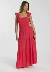 Maxiklänning i korall, med smockad byst, volangärmar och lager-på-lager kjol av lätt tyg med en subtil textur.