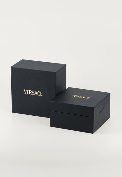 Mustad mustrid kinkepakid, millel on kuldne "VERSACE" logo ees. Üks karp on ruudukujuline, teine ristkülikukujuline, paigutatud nurga alla.
