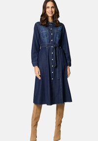 Denim shirtjurk met lange mouwen, knoopsluiting, twee borstzakken, nauwsluitende taille met riem en een knie-lange A-lijn rok in donkerblauw.