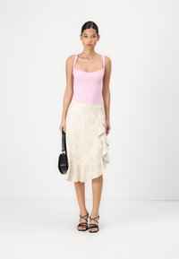 Lichtroze aansluitende body met vierkante halslijn, gecombineerd met een crèmekleurige rok met ruches en bloemenpatroon, vergezeld van zwarte sandalen met bandjes.