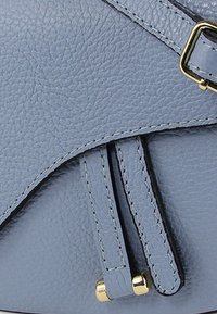 Zachte blauwe leren tas met een gestructureerd oppervlak, gouden hardware accenten en dunne, decoratieve riemen. Hoekig ontwerp met gestikte details.