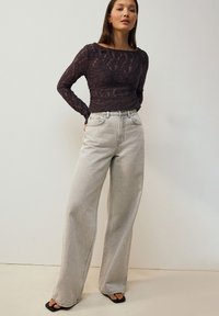 Halenka s krajkovým vzorem a dlouhými rukávy v tmavě fialové barvě spárovaná s kalhotami s vysokým pasem a širokými nohavicemi v světle šedé; měkká látka s viditelnými stehami.