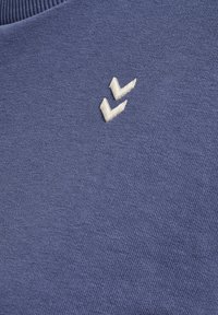 Blauwe stof met een klein wit geborduurd dubbel chevron-logo vlakbij de geribbelde halslijn.