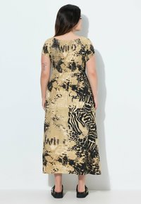 Robe maxi beige et noire à imprimé animal, avec un corsage smocké, des manches courtes et une jupe fluide. Les accents incluent un design de texte 'WILD'.